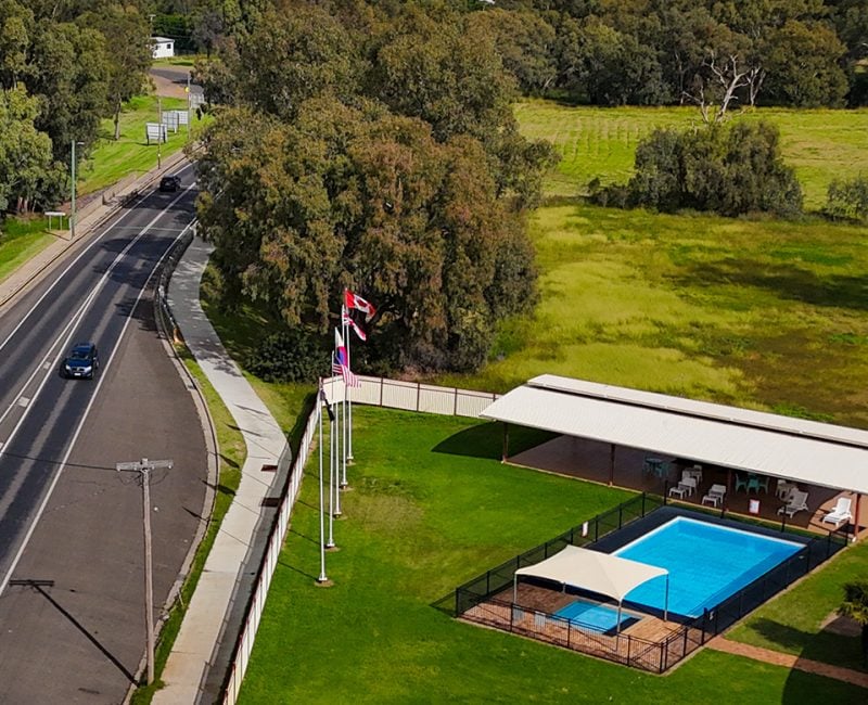 An elevated wide shot looking down a straight, multi-lane highway that cuts through a predominantly green, wooded landscape and Nandewar Motor Inn sign under a dramatic blue sky with white clouds.
