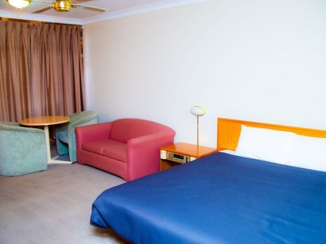A view of a Nandewar Motor Inn room with a bed in the foreground covered by a navy blue bedspread and white linens.