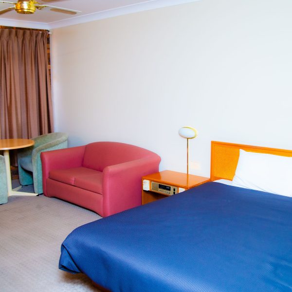A view of a Nandewar Motor Inn room with a bed in the foreground covered by a navy blue bedspread and white linens.