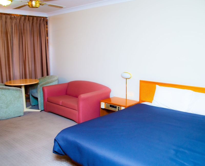 A view of a Nandewar Motor Inn room with a bed in the foreground covered by a navy blue bedspread and white linens.