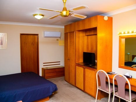 A view inside a Nandewar Motor Inn room featuring a bed with a navy blue bedspread on the left.