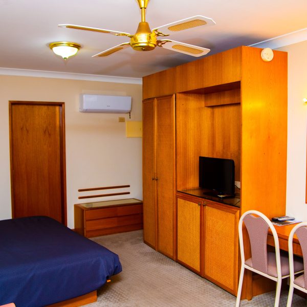 A view inside a Nandewar Motor Inn room featuring a bed with a navy blue bedspread on the left.