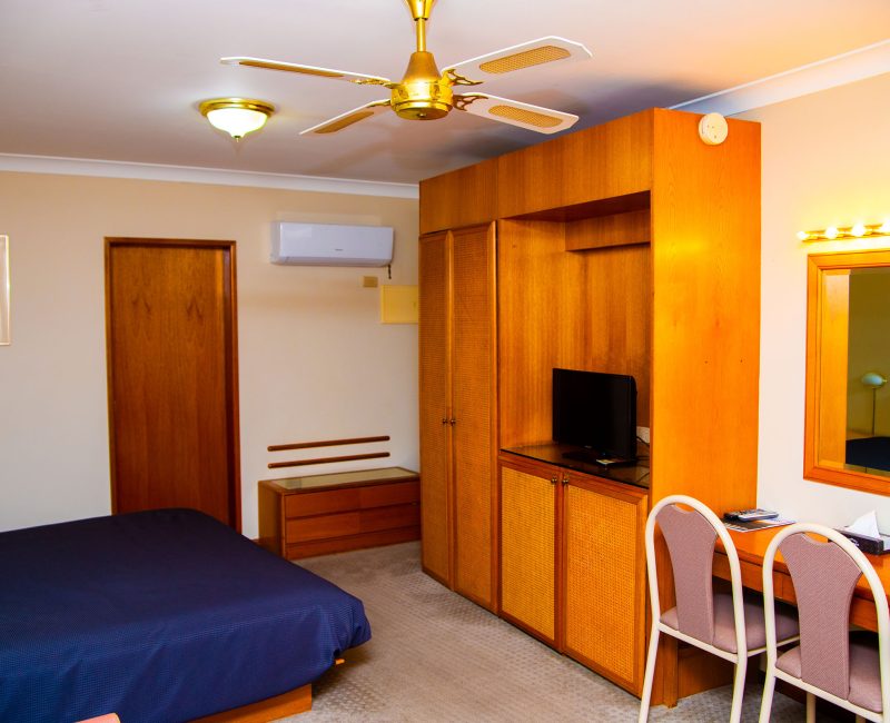 A view inside a Nandewar Motor Inn room featuring a bed with a navy blue bedspread on the left.