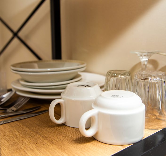 A close-up view of a wooden shelf with a black metal frame, holding kitchenware in Nandewar Motor Inn