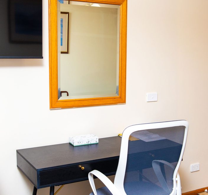 A small black desk with a gold drawer pull is positioned against a light beige wall.