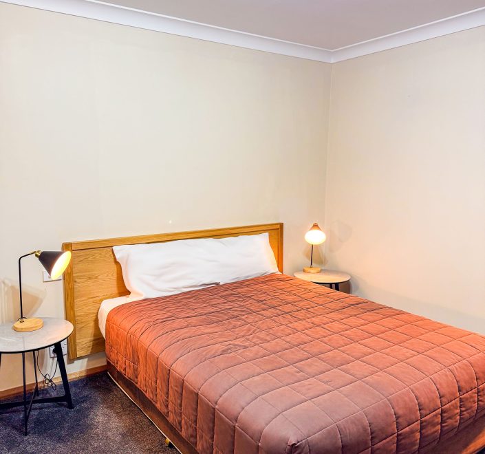 A double or queen-sized bed with a light-brown wooden headboard and a mauve or dusty-rose quilted comforter.