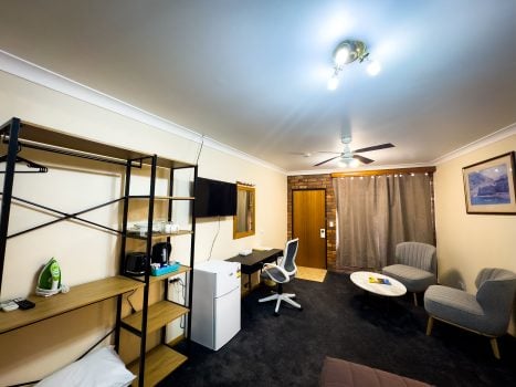 A wide-angle view of Nandewar Motor Inn's room with light beige walls and dark gray carpet. The room is well-furnished with various amenities.
