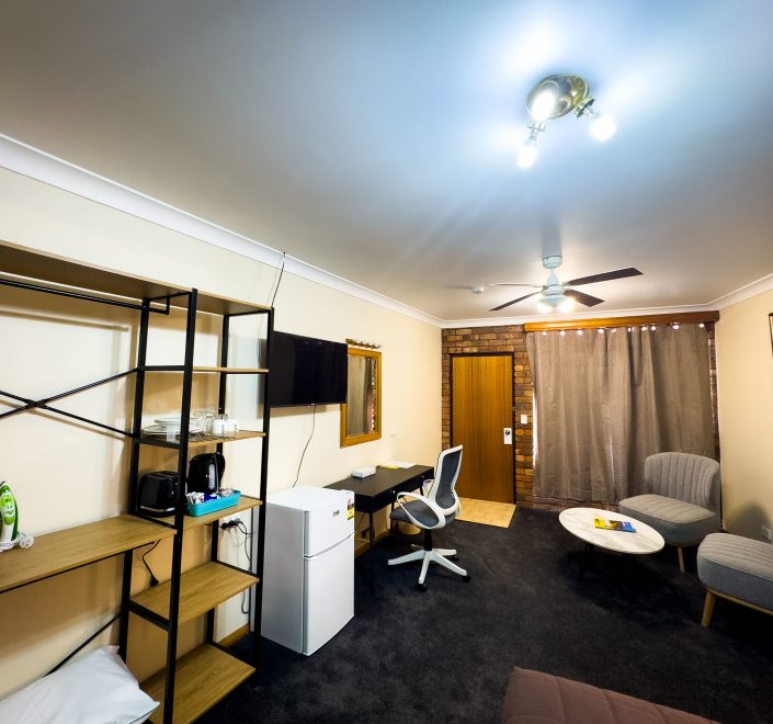A wide-angle view of Nandewar Motor Inn's room with light beige walls and dark gray carpet. The room is well-furnished with various amenities.