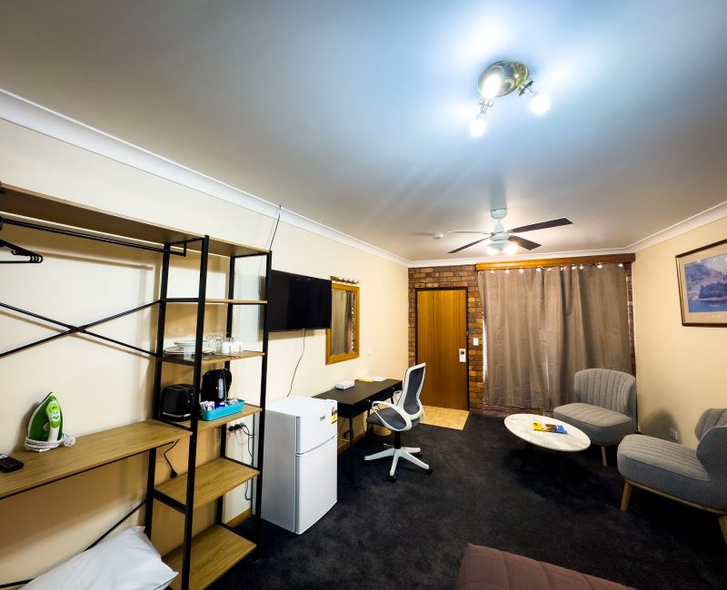 A wide-angle view of Nandewar Motor Inn's room with light beige walls and dark gray carpet. The room is well-furnished with various amenities.