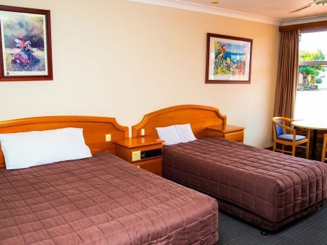 A view inside Nandewar Motor Inn's room featuring two single or double beds with matching brown quilted comforters and white pillows.