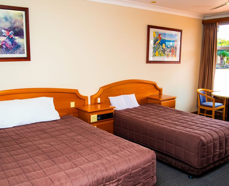 A view inside Nandewar Motor Inn's room featuring two single or double beds with matching brown quilted comforters and white pillows.