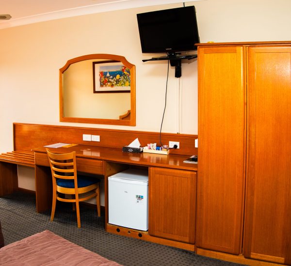 A large, built-in wooden unit with a honey-colored finish spans the width of the image, serving as a desk, cabinet, and wardrobe.