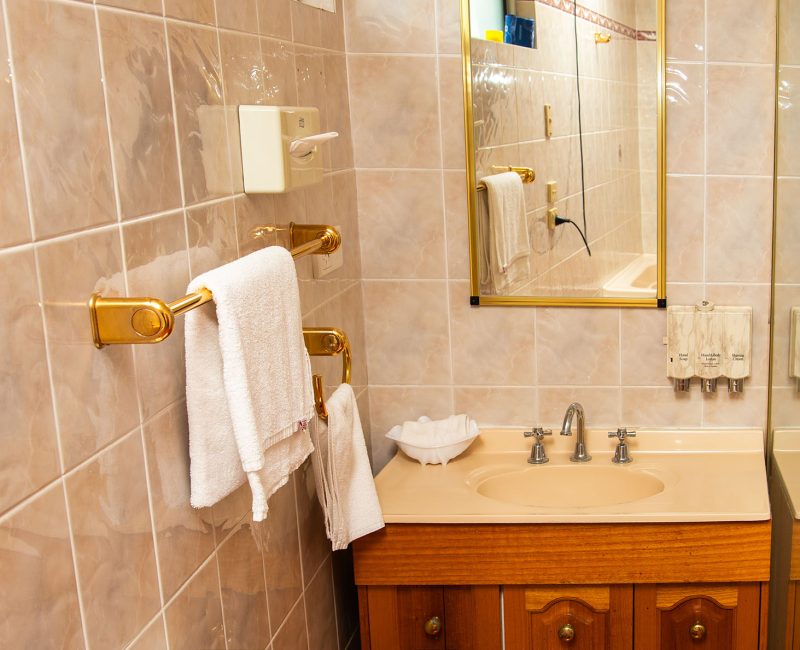 A bathroom featuring a wooden vanity cabinet with gold-toned drawer pulls and a light peach or beige countertop and integrated sink.
