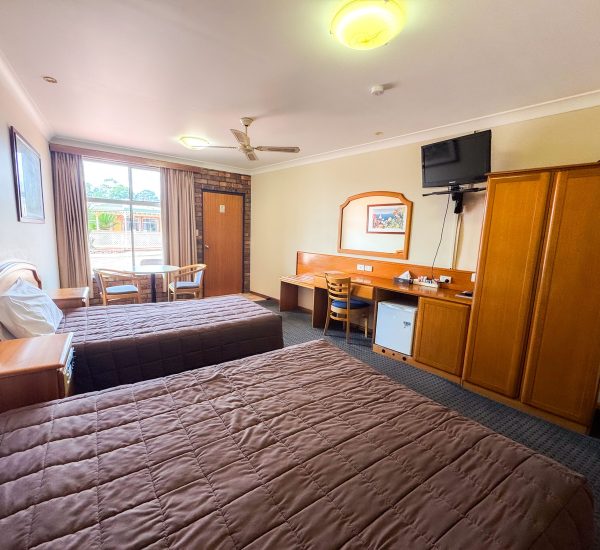 A wide-angle view of Nandewar Motor Inn room featuring two single or double beds in the foreground, each covered with a brown quilted comforter and white pillows.