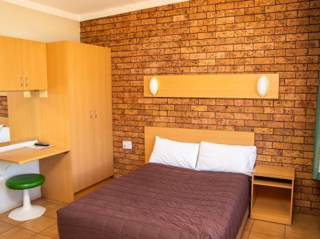 Nandewar Motor Inn's room featuring a double or queen-sized bed with a dark brown quilted comforter and white pillows, set against a light wood headboard.