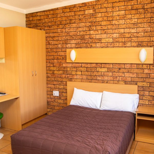 Nandewar Motor Inn's room featuring a double or queen-sized bed with a dark brown quilted comforter and white pillows, set against a light wood headboard.