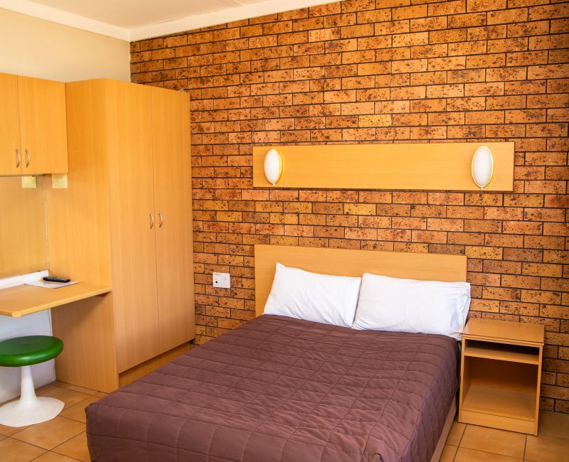 Nandewar Motor Inn's room featuring a double or queen-sized bed with a dark brown quilted comforter and white pillows, set against a light wood headboard.