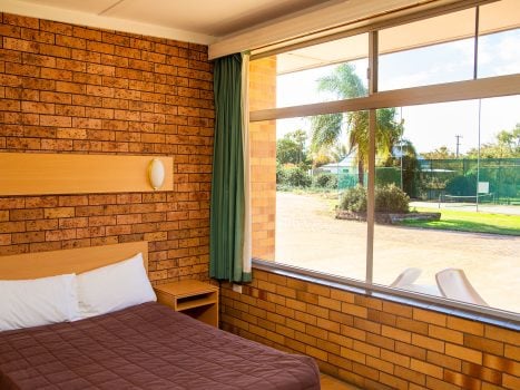 Nandewar Motor Inn room interior featuring a bed with a dark brown quilted comforter and white pillows, tucked against a light wood headboard.