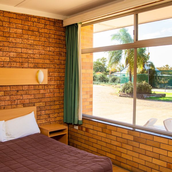Nandewar Motor Inn room interior featuring a bed with a dark brown quilted comforter and white pillows, tucked against a light wood headboard.