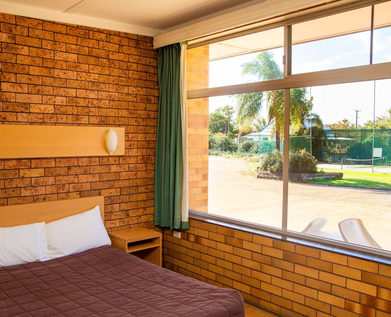 Nandewar Motor Inn room interior featuring a bed with a dark brown quilted comforter and white pillows, tucked against a light wood headboard.