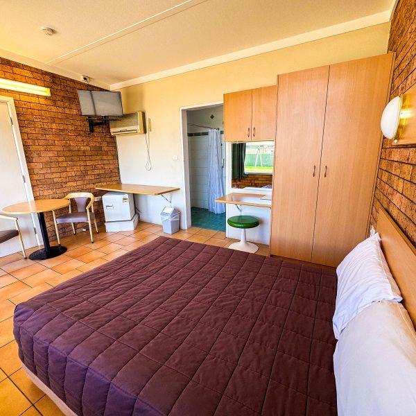 Nandewar Motor Inn room featuring a large bed in the foreground with a dark brown or deep purple quilted comforter and a single white pillow.