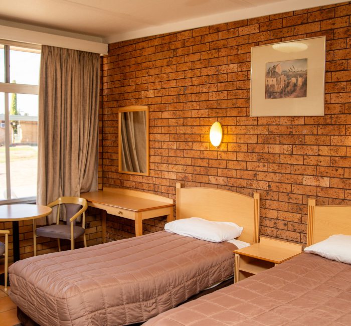 The interior of a motel room designed for two guests, featuring a prominent brick wall and a window view.