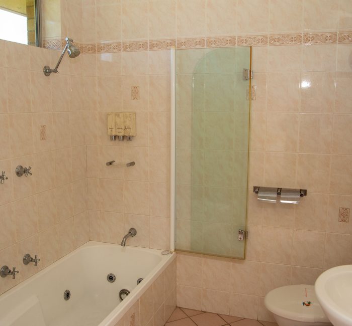 Nandewar Motor Inn's bathroom interior with walls covered in large, light beige or pale pink marbled tiles.