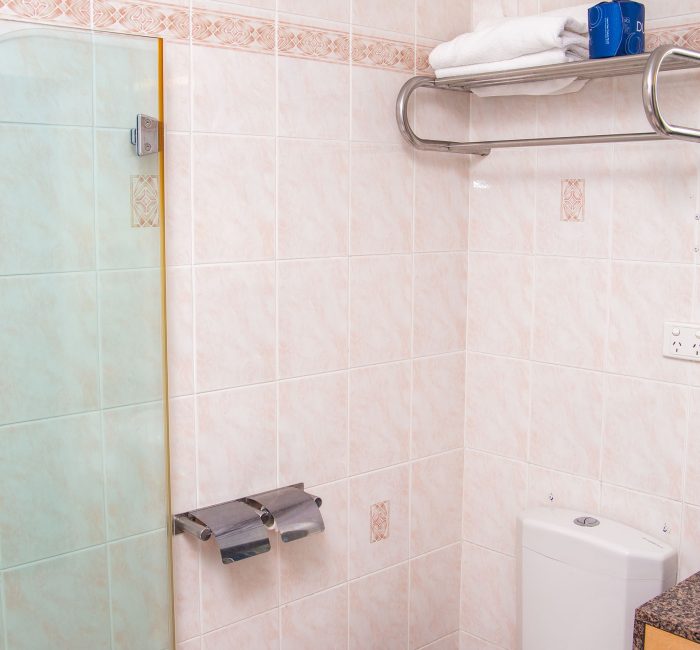 A close-up of the toilet and towel storage area in a motel bathroom.