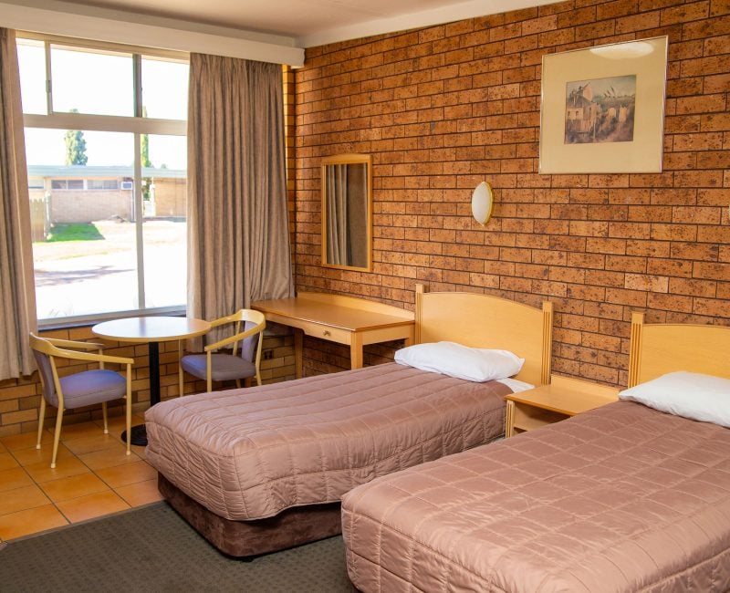 Nandewar Motor Inn room featuring two single beds with mauve or brownish-pink quilted comforters and light wood headboards.