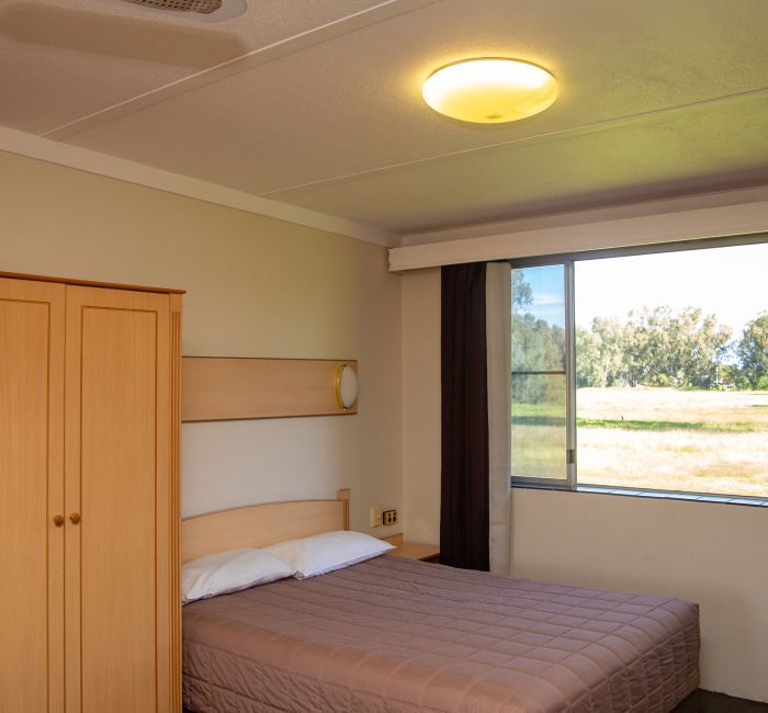 A motel room, focusing on the sleeping area, storage, and a large window view.