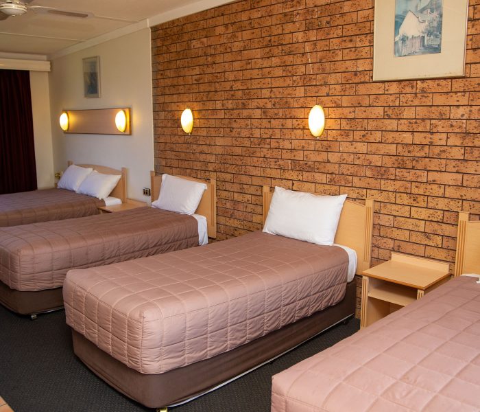 A wide-angle view of a motel room containing four single beds lined up in a row.