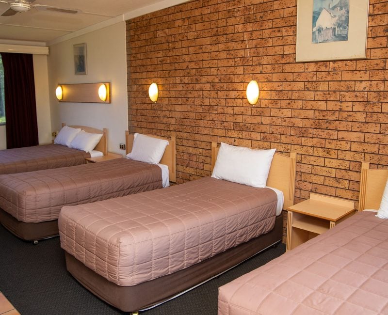 A wide-angle view of a motel room containing four single beds lined up in a row.