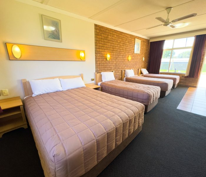 A wide-angle view of Nandewar Motor Inn room containing four beds lined up along a wall.