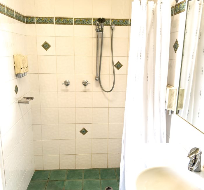 A bathroom interior with walls covered in large, white or off-white square tiles.