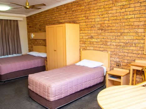 Nandewar Motor Inn's room featuring two single or double beds with dusty-rose or mauve quilted comforters and white pillows.