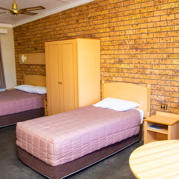 Nandewar Motor Inn's room featuring two single or double beds with dusty-rose or mauve quilted comforters and white pillows.
