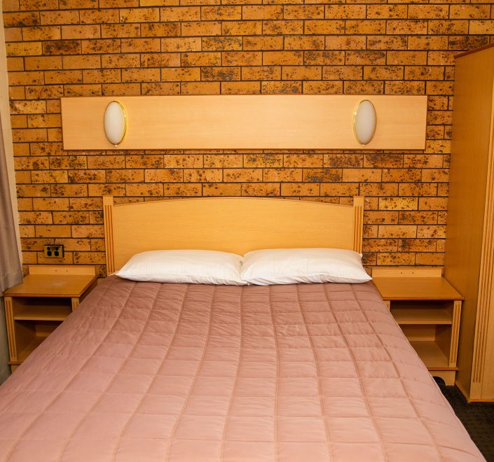 A straight-on view of the bed and storage area in a Nandewar Motor Inn's room.