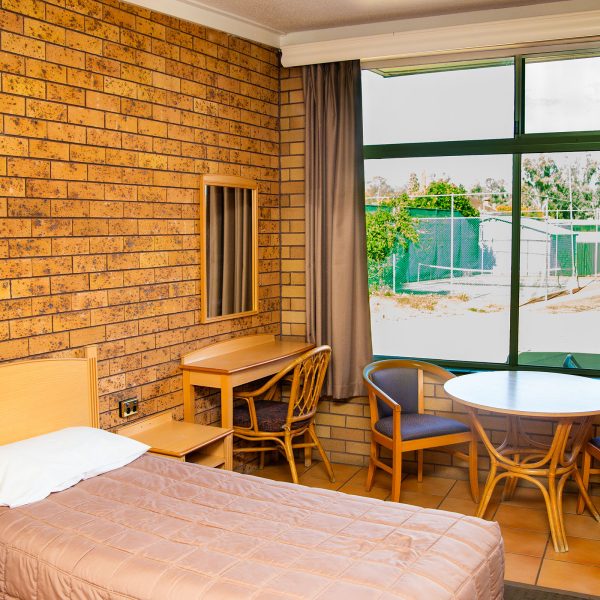 Cozy Nandewar Motor Inn room with bed and table by window.