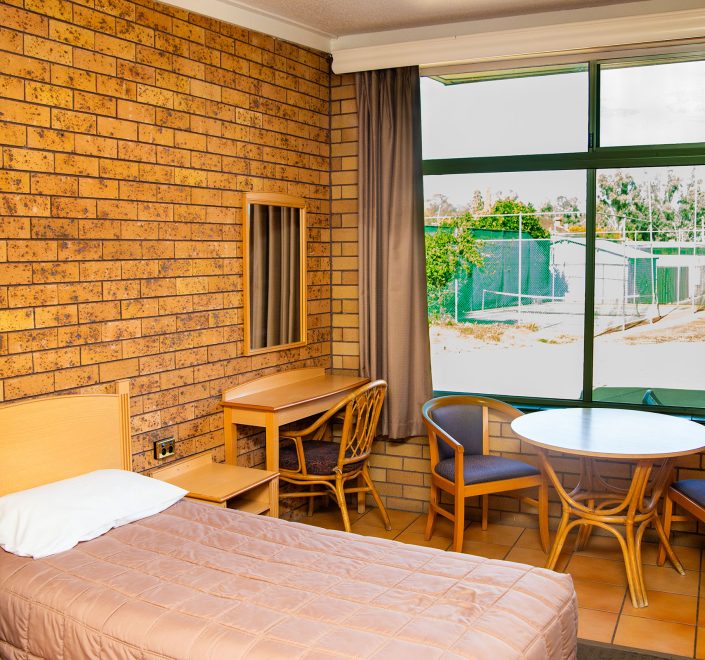Cozy Nandewar Motor Inn room with bed and table by window.