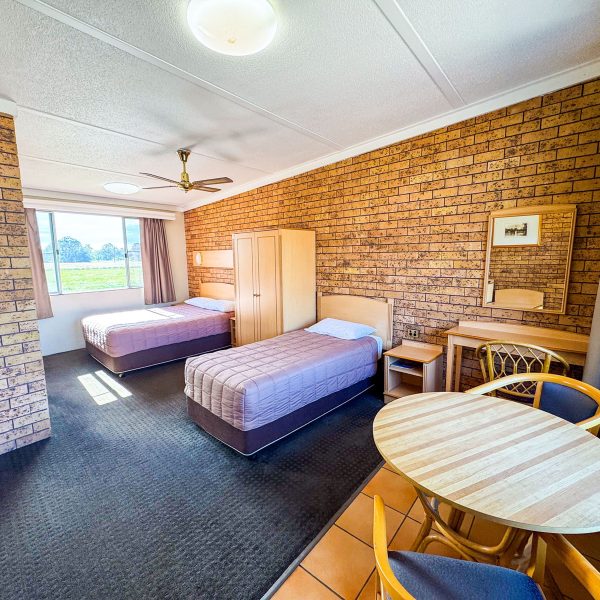 A wide-angle view of Nandewar Motor Inn's room with two single or double beds, both covered with dusty-rose or mauve quilted comforters and white pillows.