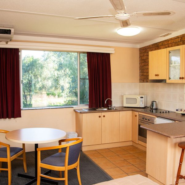 A wide-angle view of a motel room with an integrated sleeping (foreground, partially visible), dining, and kitchenette area.