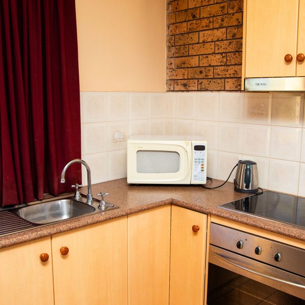 A bright, L-shaped kitchenette featuring light wood cabinetry and a speckled brown countertop.