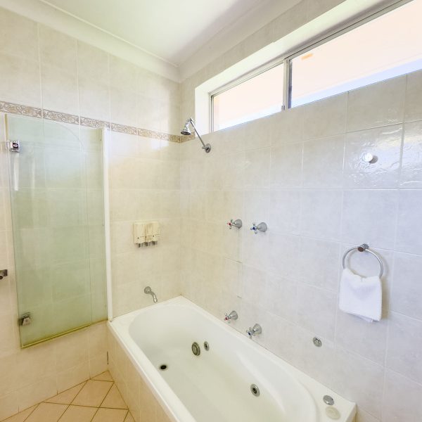 A brightly lit, tiled bathroom featuring a combined tub and shower area.