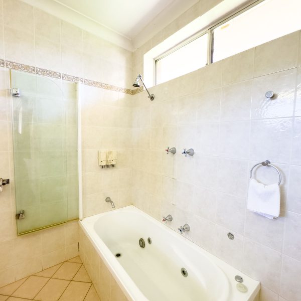 A bathroom area with walls covered in large, square, light beige or off-white marbled tiles with white grout.