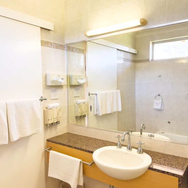 A bathroom vanity featuring a white, oval drop-in sink with chrome fixtures, set into a wooden counter with a speckled brown and white granite-look top.