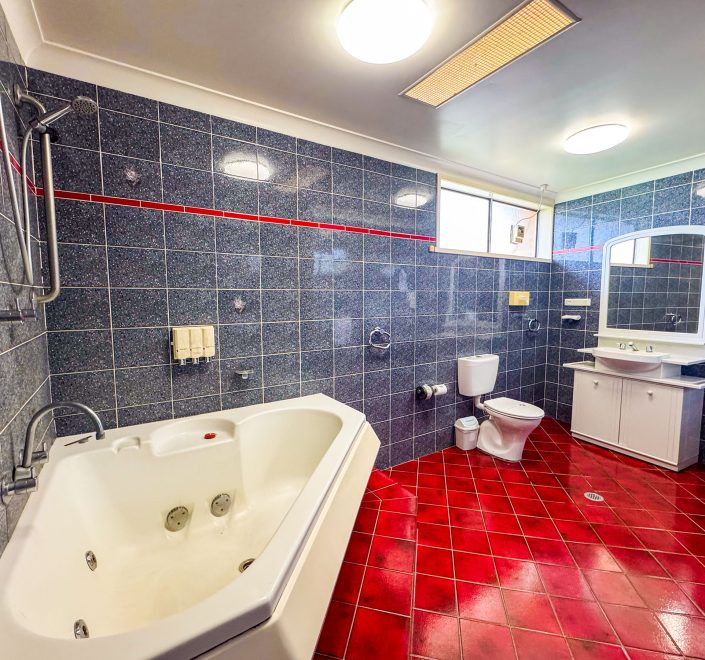 A large bathroom featuring striking dark blue or gray marbled square wall tiles and contrasting glossy red square floor tiles.