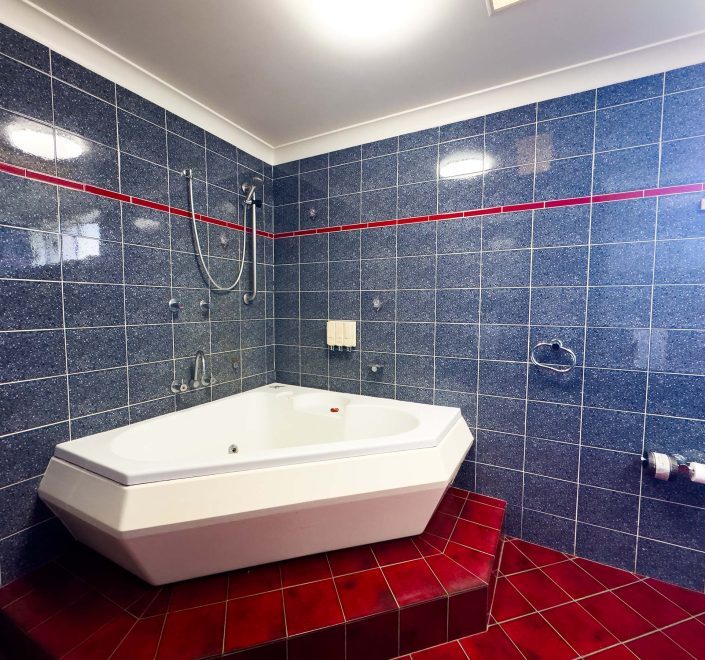 A large, white corner spa tub is built on a raised step platform covered in glossy red square tiles.